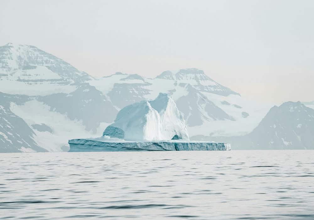 Arctic Desert Iceberg Floating in Cold Ocean with Snowy Mountains